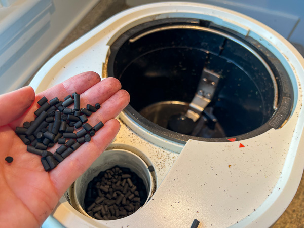 Lomi filter refill pellets, made of activated charcoal, in the review writer's hand above the Lomi composter machine. ©KettiWilhelm2023