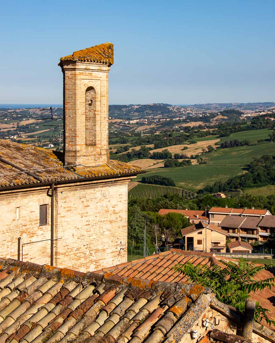 Ancient brick buildings bathed in golden hour light stand in front of the rolling hills we've been biking through in Marche, Italy. ©KettiWilhelm2023