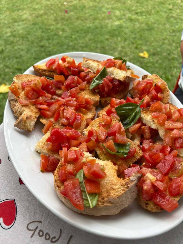 A plate of bruschetta, toasted bread with tomatoes and basil, to eat with the fresh olive oil from the olive groves behind us at this stop on our electric bike tour in Italy's Marche region. ©KettiWilhelm2023