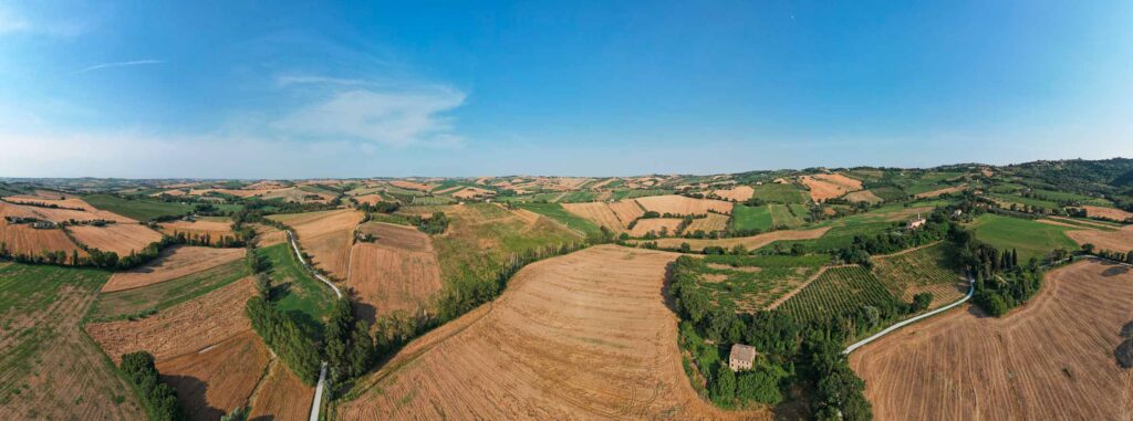 Farm fields in rural Marche, Italy, photographed from a drone showing the area of our bike tour, under bright blue June skies.  ©KettiWilhelm2023