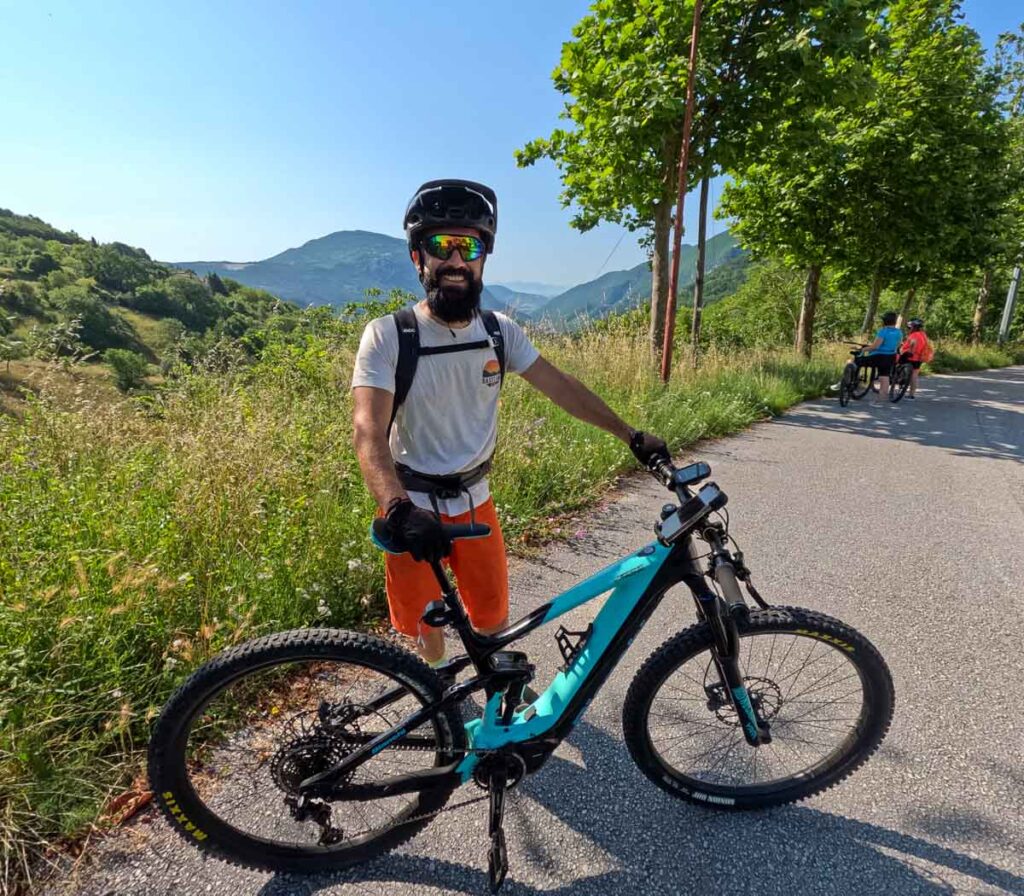 Marco, our local Italian guide for this excellent Marche by bike tour, standing behind his Bianchi brand Italian e-bike, with the blue mountains of rural Italy in the background. ©KettiWilhelm2023