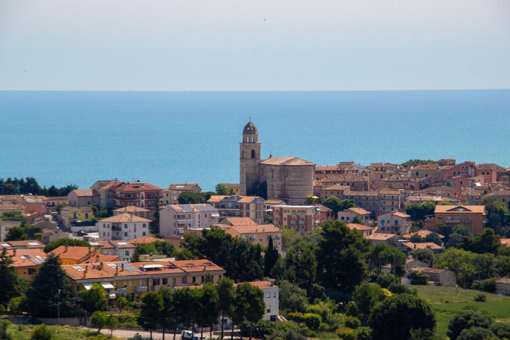 The historic center of Sirolo, Marche, Italy, with a tower rising above the background of the bright blue Adriatic Sea. ©KettiWilhelm2023
