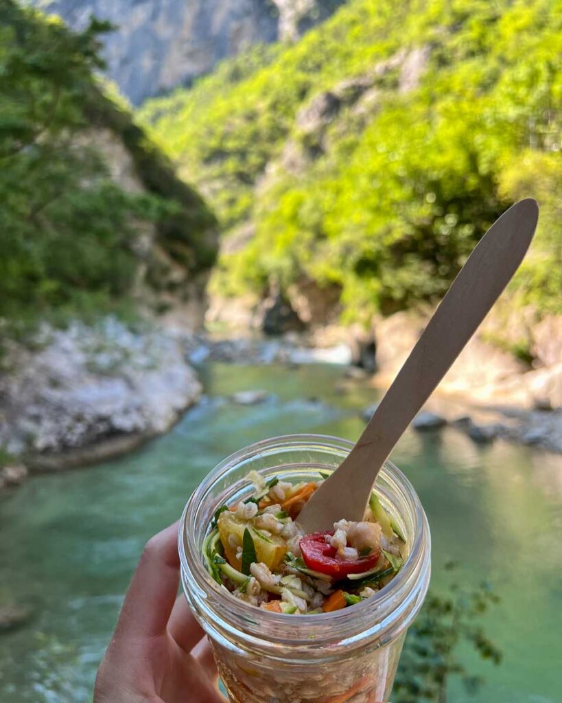 A vegetarian lunch of farro salad prepared by Basecamp523, the local tour operator for this Marche by bike tour, with a river behind. ©KettiWilhelm2023