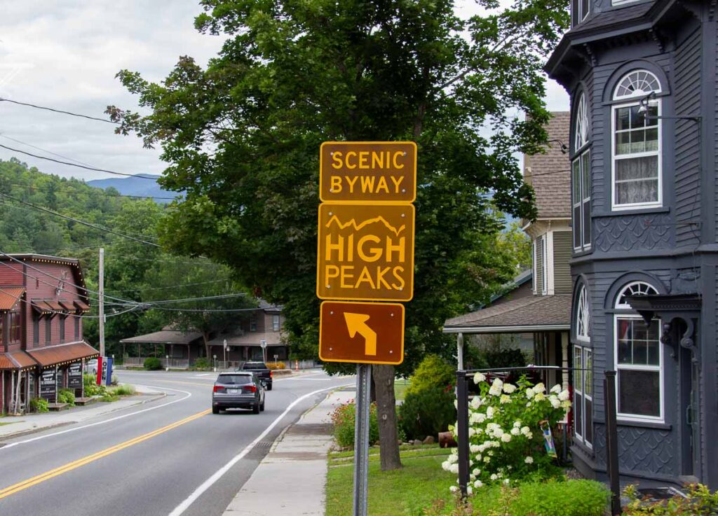 A road side reads “Scenic Byway High Peaks” with an arrowing in downtown Keene, New York, the first town on this three-day Adirondack road trip itinerary. ©KettiWilhelm2023