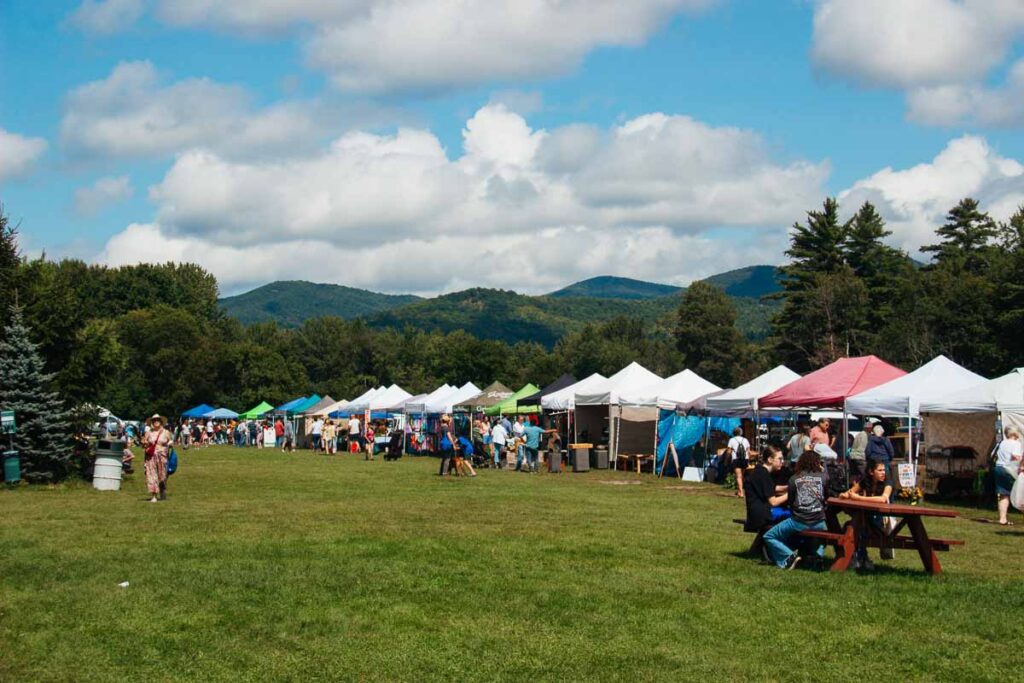 ALT A long line of tents on a field of grass at the Keene Valley Farmers’ Market, a great place to buy local souvenirs in the Adirondacks. ©KettiWilhelm2023