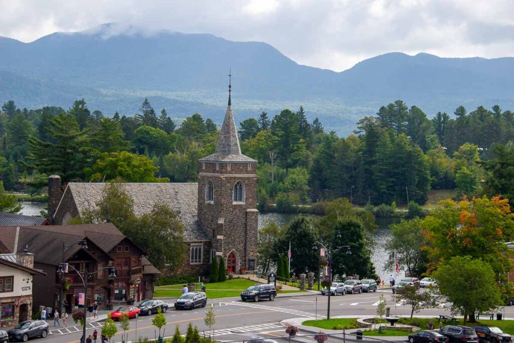 An old stone church in downtown Lake Placid, surrounded by trees and blue mountains. ©KettiWilhelm2023