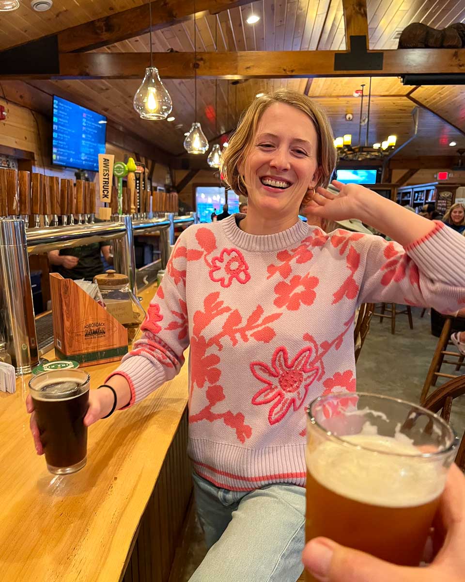 The author of this Adirondack weekend getaway guide toasting her husband with a dark beer at Raquette River Brewing – a great local spot in the Adirondacks. ©KettiWilhelm2023