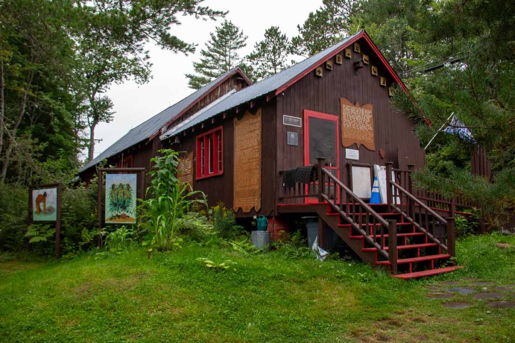 The Six Nations Iroquois Cultural Center, an excellent local museum in the Adirondacks, seen from outside – a small brown building surrounded by green grass and trees. ©KettiWilhelm2023