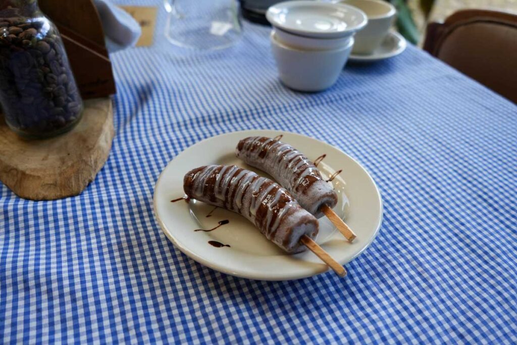 Two chocobananas with wooden – not plastic – sticks (chocolate covered bananas, popular in Central America) on a plate at a coffee shop in Ataco de Concepción. ©KettiWilhelm2023