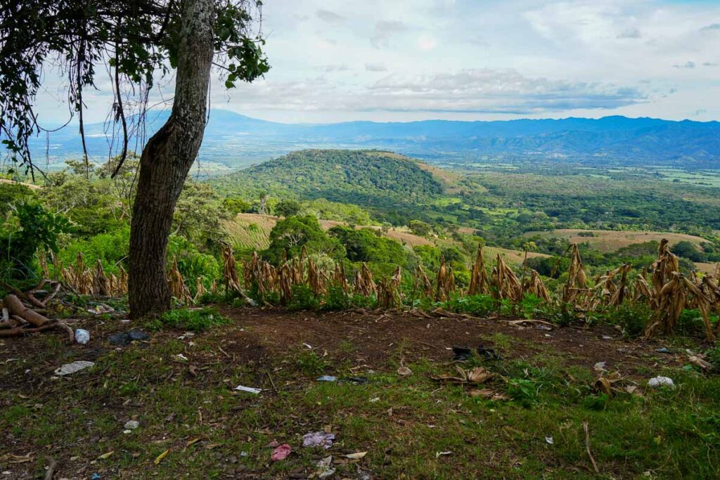Plastic water bottles and other little scatter the roadside in front of a view of farm fields and mountains in the distance in Santa Ana, El Salvador. ©KettiWilhelm2023