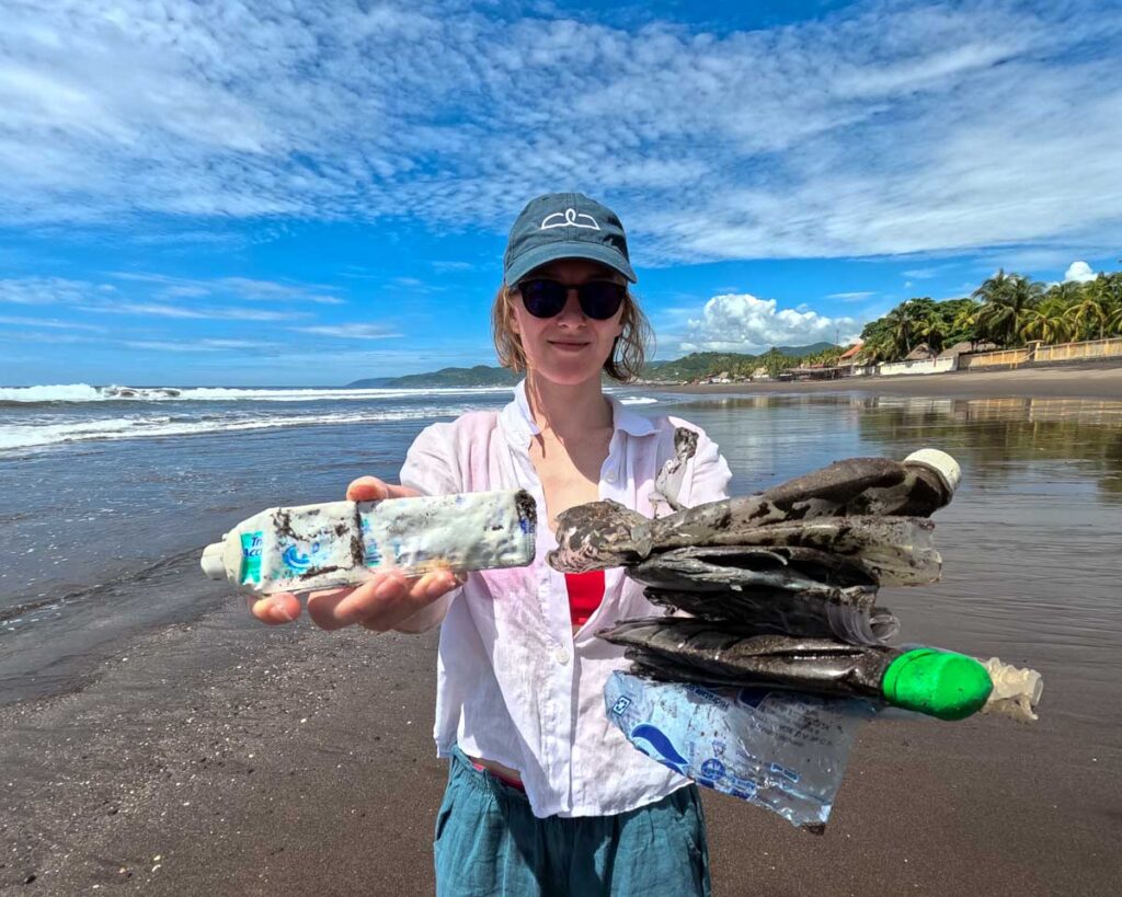 Ketti Wilhelm, the sustainable travel writer who wrote this story, collecting garbage, including a toothpaste tube and many plastic water bottles, on a beach in El Salvador. ©KettiWilhelm2023