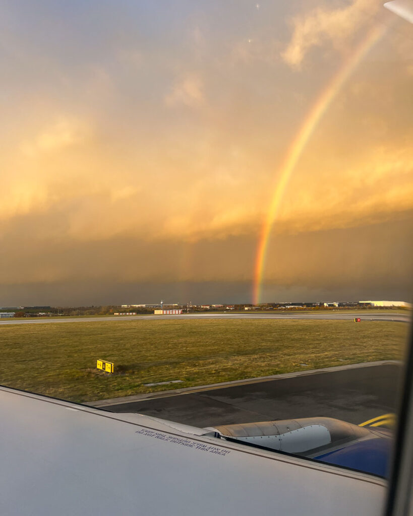 Rainbow on the airport tarmac, seen from airplane window seat. ©KettiWilhelm2023