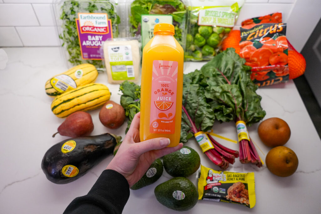 Organic, cold pressed orange juice from the Imperfect Foods brand, in a perfectly good-looking bottle, in front of the rest of my weekly home grocery delivery from Misfits Market. ©KettiWilhelm2024