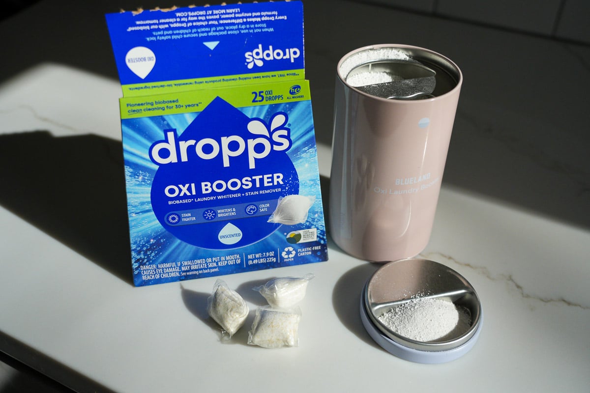 Dropps oxi booster laundry pods and Blueland oxibooster laundry powder, both in plastic-free packaging, sitting on the writer's kitchen countertop. ©KettiWilhelm2025