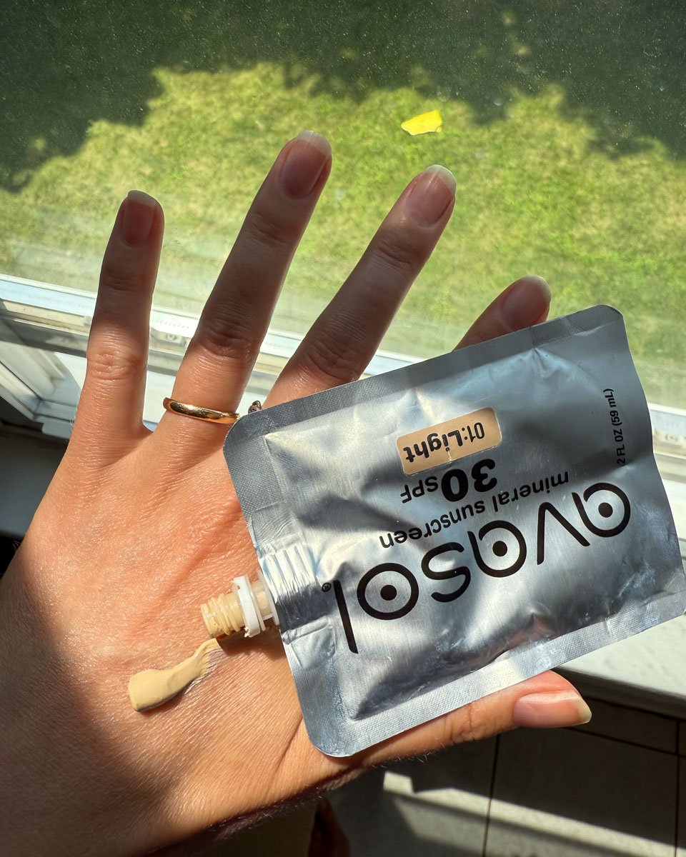 The hand of author of this Avasol sunscreen review, with a bit of Avasol's "Environmental Defense Cream" tinted mineral sunscreen cream in the "light" shade on her hand along with the aluminum pouch the sunscreen comes in. ©KettiWilhelm2025