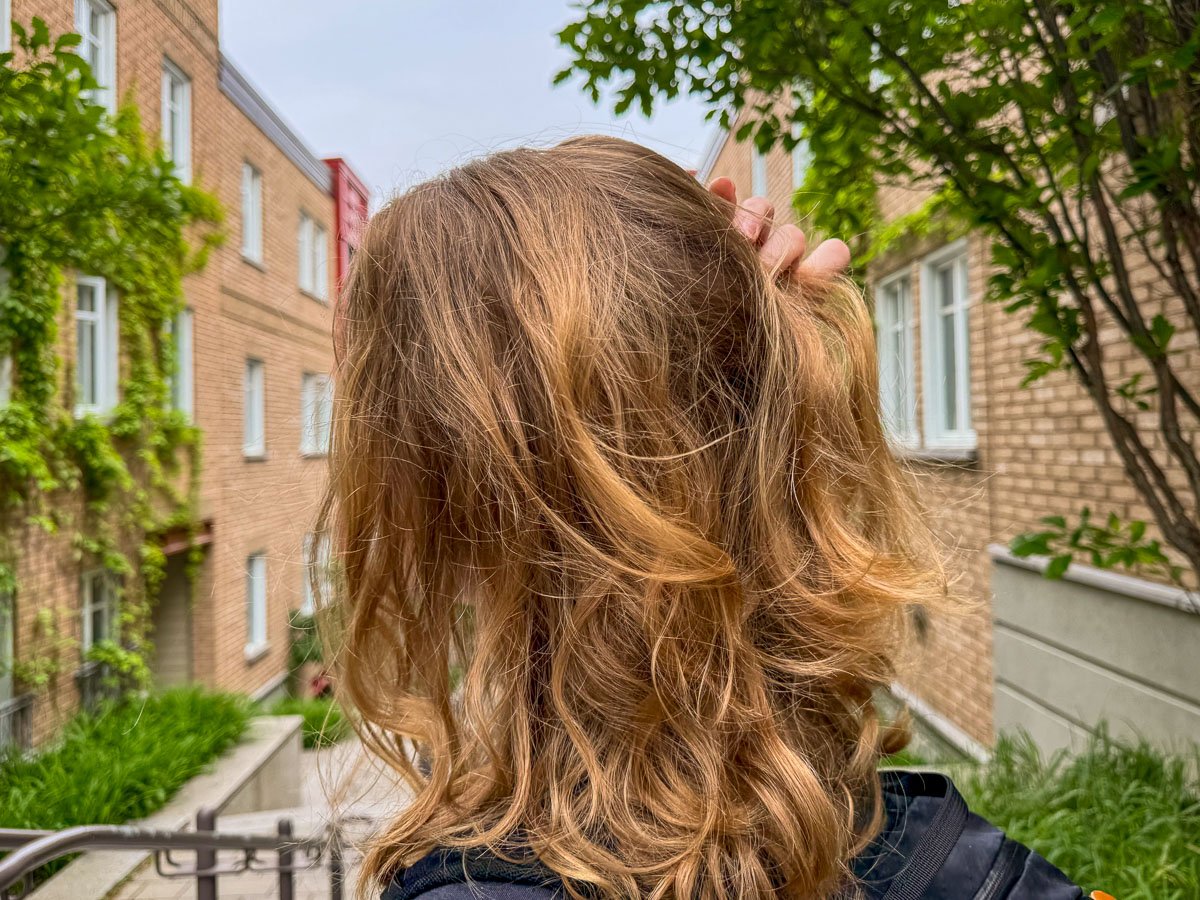 The author of this Dip review (a white woman in her 30s with strawberry blonde, shoulder-length hair) runs her hand through her hair after washing it with Dip shampoo and conditioner bars. Her hair is a bit frizzy from humidity, and lightly shiny without any added product or styling. ©KettiWilhelm2025