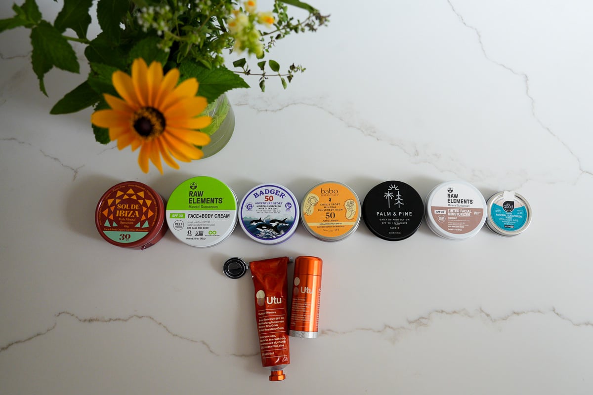 The collection of plastic-free, organic sunscreens in metal packaging that we tested for these reviews, including tinted and untinted mineral sunscreens from Sol de Ibiza, Raw Elements, Badger, Babo Botanicals, Palm and Pine, All Good, and Utu. ©KettiWilhelm2025