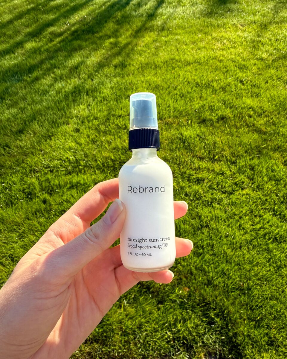 Holding a bottle of Rebrand Skincare's refillable, mineral sunscreen for face, which is the SPF with the least white cast I've tested. ©KettiWilhelm2026