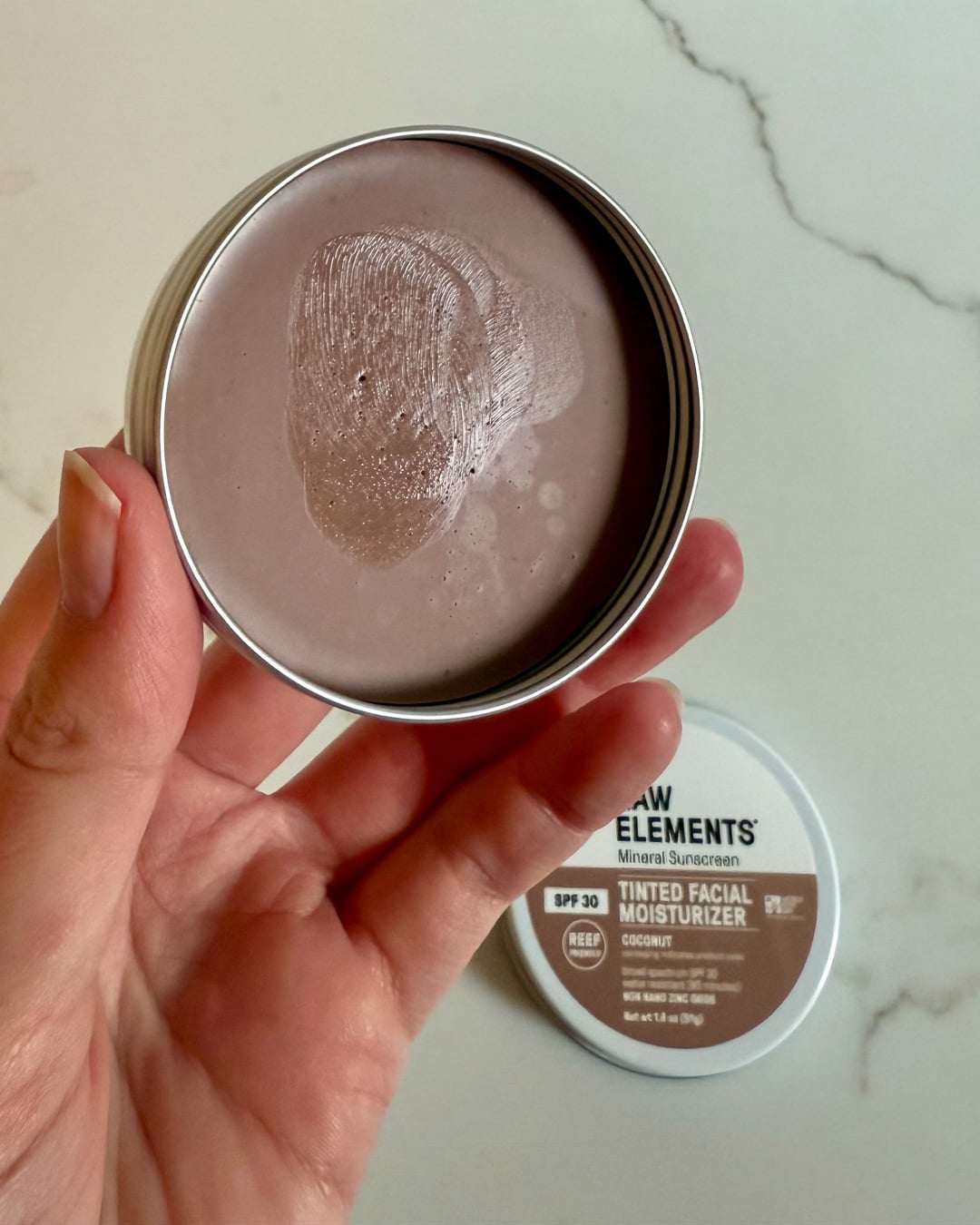 My open tin of Raw Elements tinted facial sunscreen in the "coconut" shade, which looks like a medium brown, but rubs in well on my fair skin and works great as a mineral suncreen for body, too. ©KettiWilhelm2026