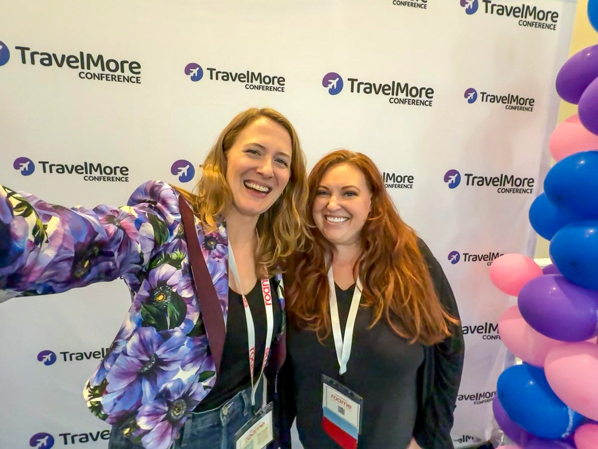 Sustainable travel blogger Ketti Wilhelm stands with Ashley Peterson, the founder of Travel More conference, in front of the "red carpet" banner at TravelMore where Ashley taught about points and miles for beginners and experts. ©KettiWilhelm2025