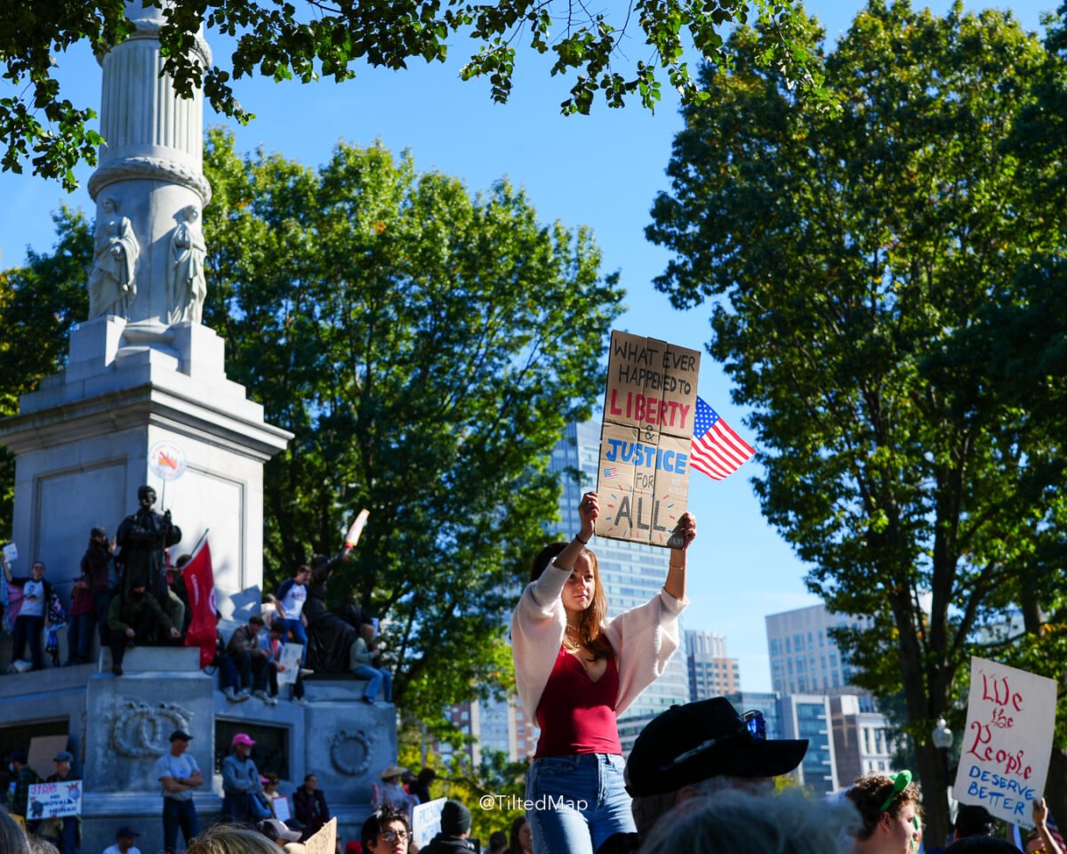 A young woman holds a sign reading "whatever happened to liberty and justice for all" along with a US flag, during the No Kings protest against President Donald Trump and ICE in Boston in October, 2025. ©KettiWilhelm2025