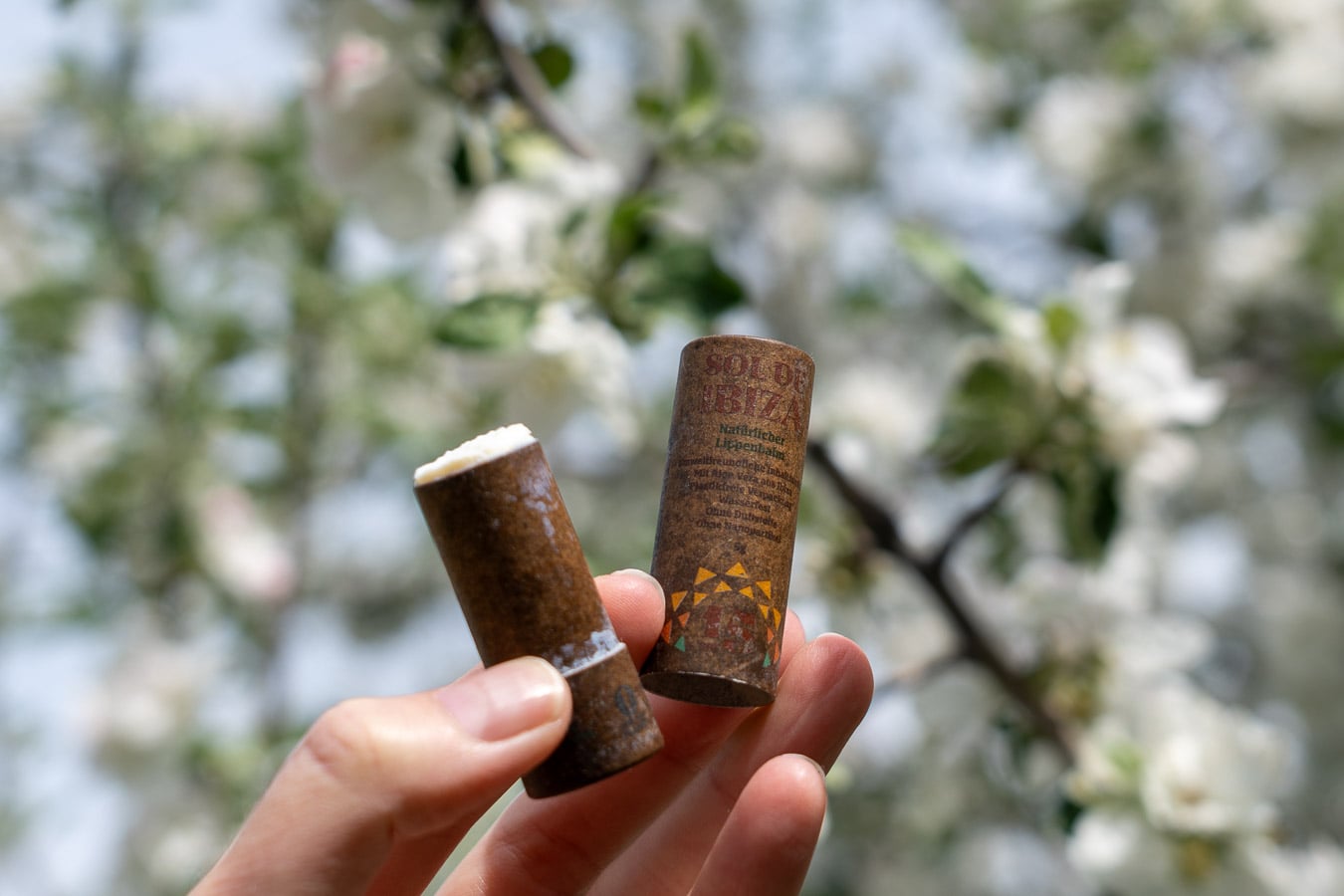 Cardboard tube of SPF 30, the best organic lip balm with SPF, from Sol de Ibiza, a European sunscreen brand making plastic-free options that I tested in this review, in front of a tree with white flowers. ©KettiWilhelm2026