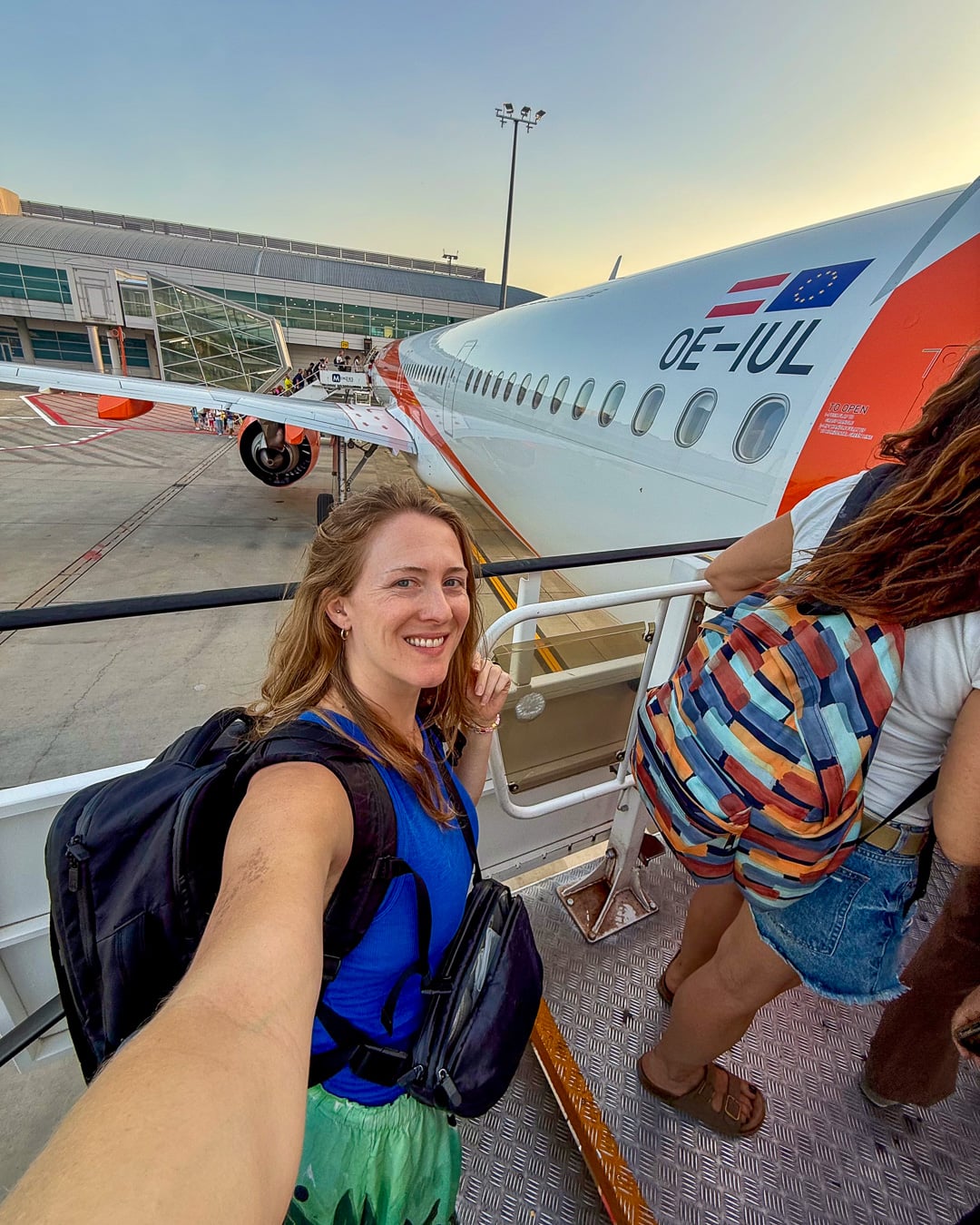 Sustainable travel writer Ketti Wilhelm, a white woman with blond hair in her 30s wearing a travel backpack, stands on the back stairway before boarding a flight in Europe. ©KettiWilhelm2026