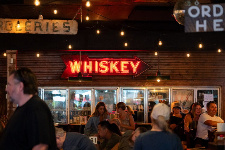 A red neon "whiskey" sign at the back of the Fox and Locke, famous for its open mic music show on Thursday nights, in Leiper's Fork, Tennessee, with local customers eating lunch. ©KettiWilhelm2026