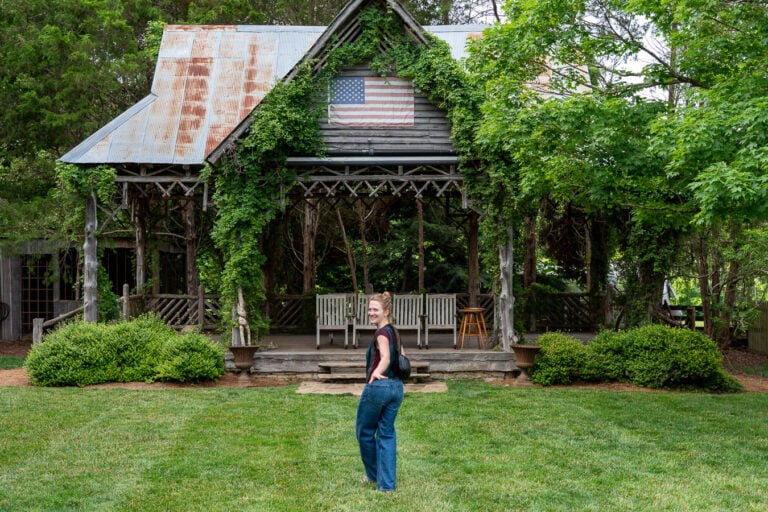 Sustainable travel writer and influencer Ketti Wilhelm, of TiltedMap.com, a white woman with blond hair wearing jeans and a t-shirt, walks toward the gazebo of the Lawn Chair Theater, adorned with a faded US flag, behind the Leiper's Creek Gallery in Leiper's Fork, Tennessee, while visiting Franklin and the surrounding area. ©KettiWilhelm2026