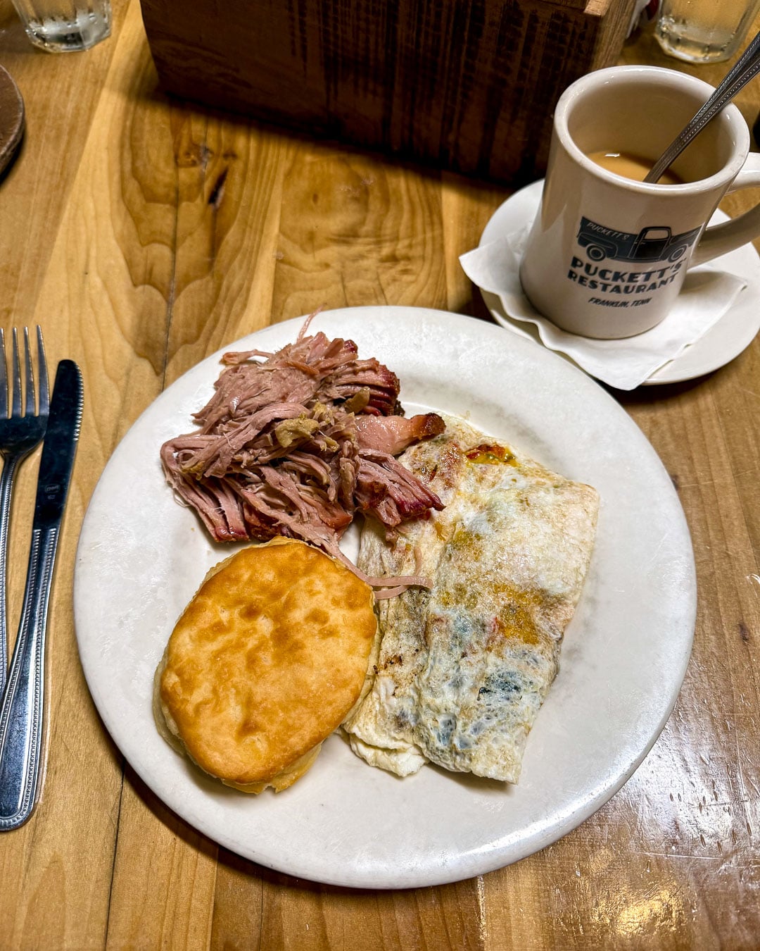 A coffee cup and plate of Southern breakfast foods - omelette, a homemade biscuit, and pulled pork at Puckett's Restaurant a classic Southern diner in Franklin, Tennessee. ©KettiWilhelm2026