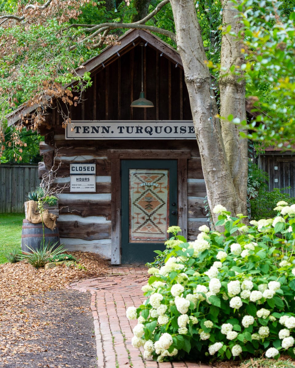 Tennessee Turquoise, a small jewelry shop in Leiper's Fork, Tennessee, surrounded by trees and white flowering bushes. ©KettiWilhelm2026